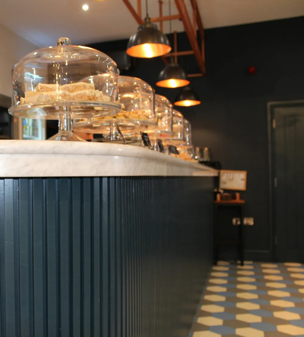 Café counter with a marble top, cakes under glass domes, small chalkboard tags and pendant lamps