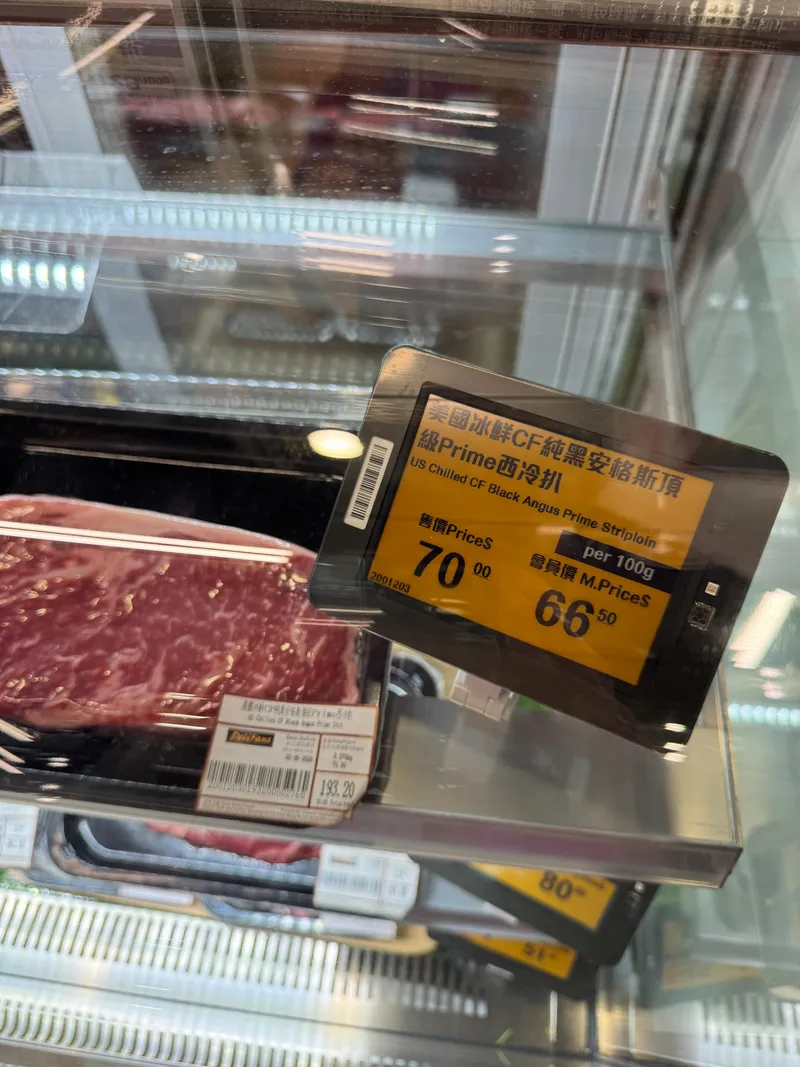 Yellow-and-black electronic shelf label showing regular and member prices per 100 g for Angus striploin in a meat chiller