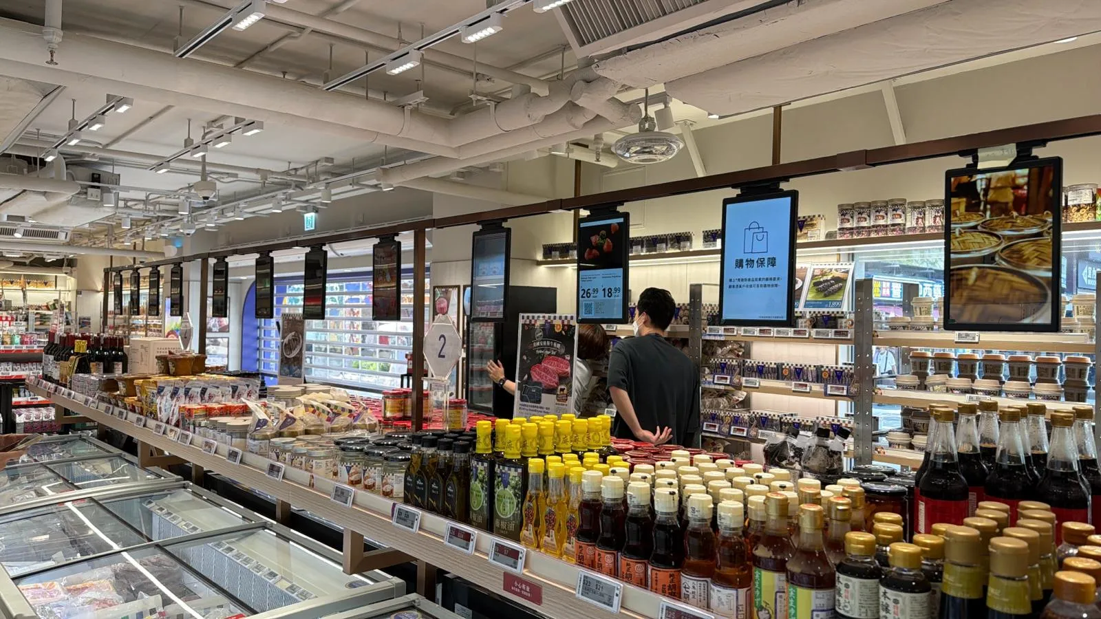 Grocery store aisle with electronic shelf labels along the shelf edges and digital displays hanging above, Hong Kong installation