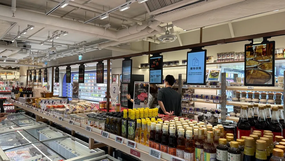 Grocery store aisle with electronic shelf labels along the shelf edges and digital displays hanging above, a Hong Kong installation