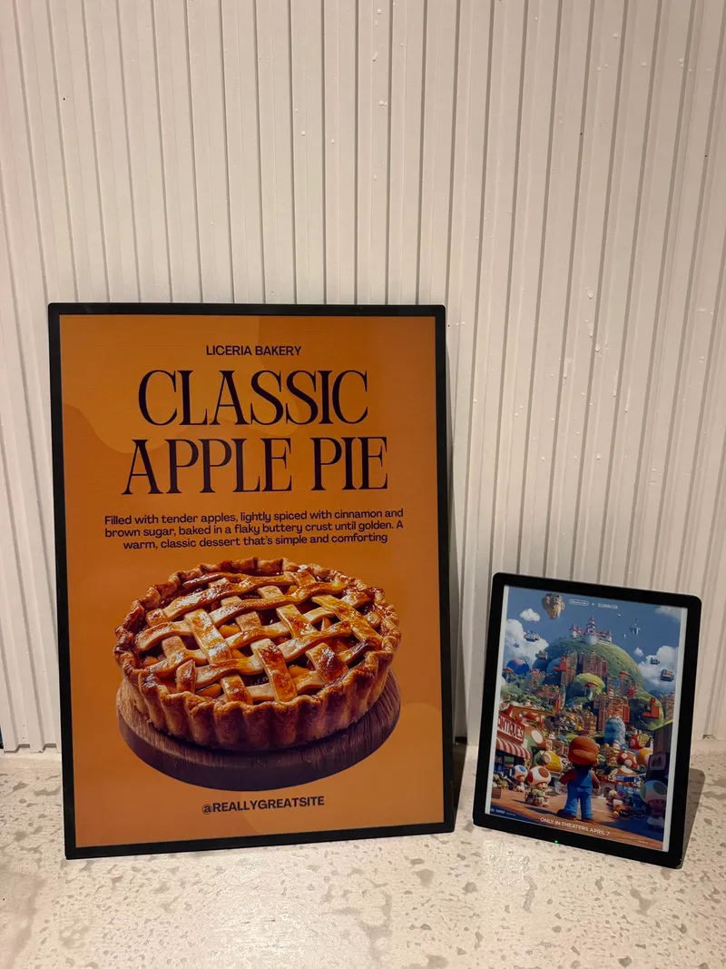 Two colour ePaper signs on a counter, a large bakery poster for apple pie beside a smaller display