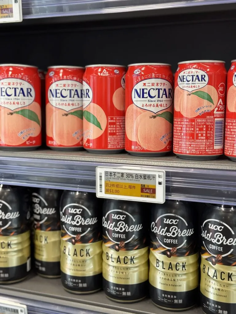 Electronic shelf label with a yellow sale panel between cans of peach nectar and bottled cold brew coffee