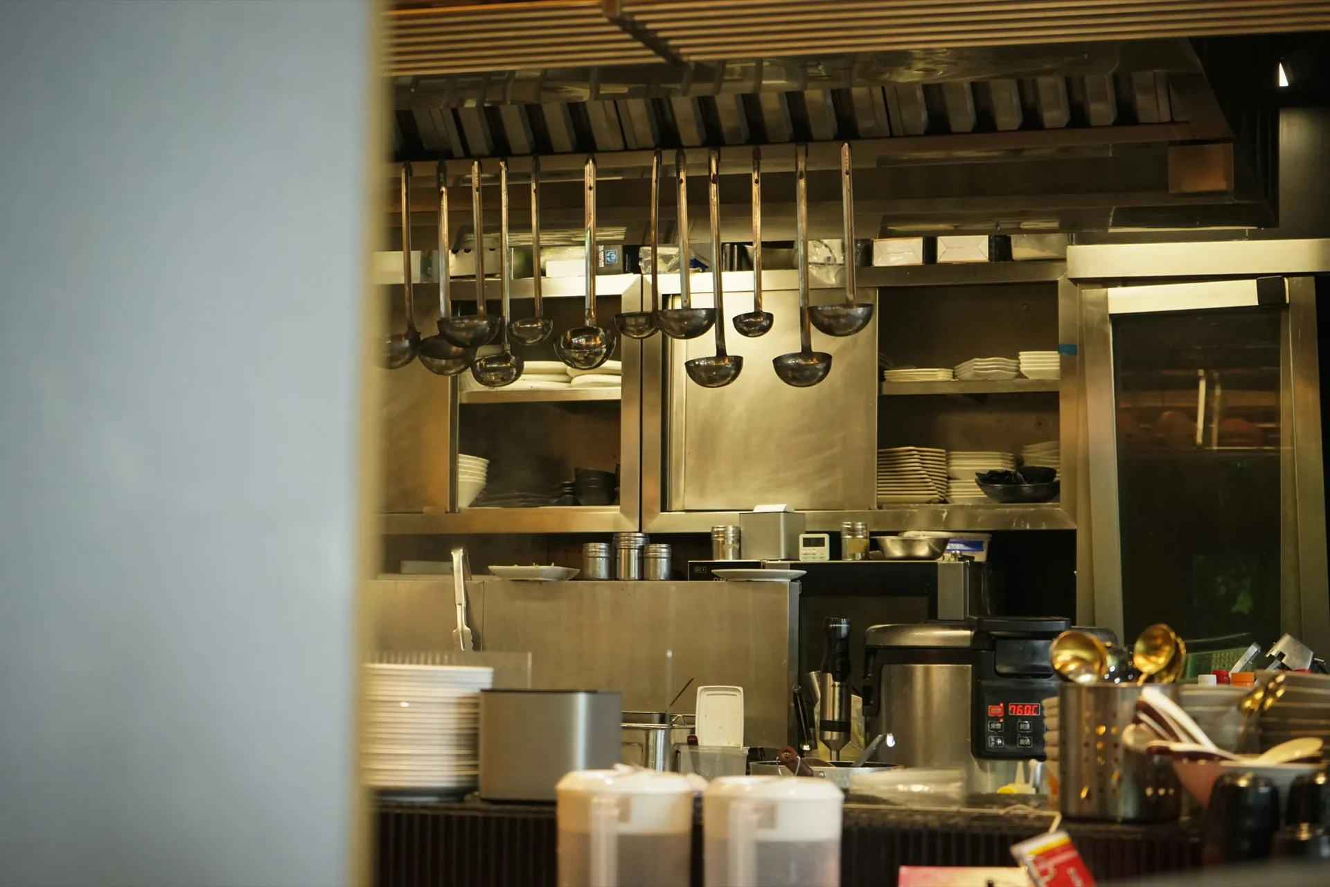 Restaurant kitchen with stainless steel shelving, stacked plates and ladles hanging above the pass