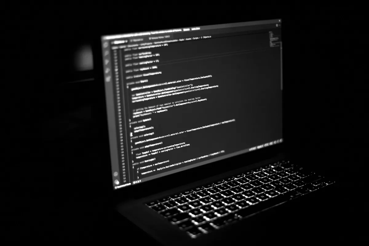 Laptop in a dark room showing program code in an editor, in black and white