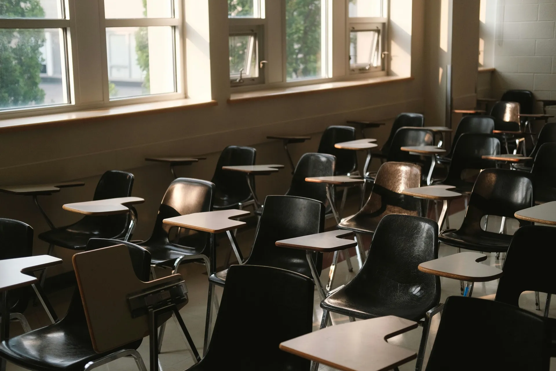 Empty university classroom with rows of tablet-arm chairs in afternoon sunlight from tall windows