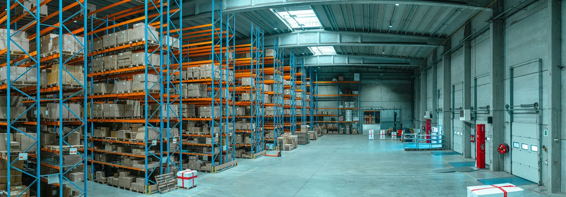 Warehouse with tall blue and orange pallet racking full of cartons beside a row of loading bay doors
